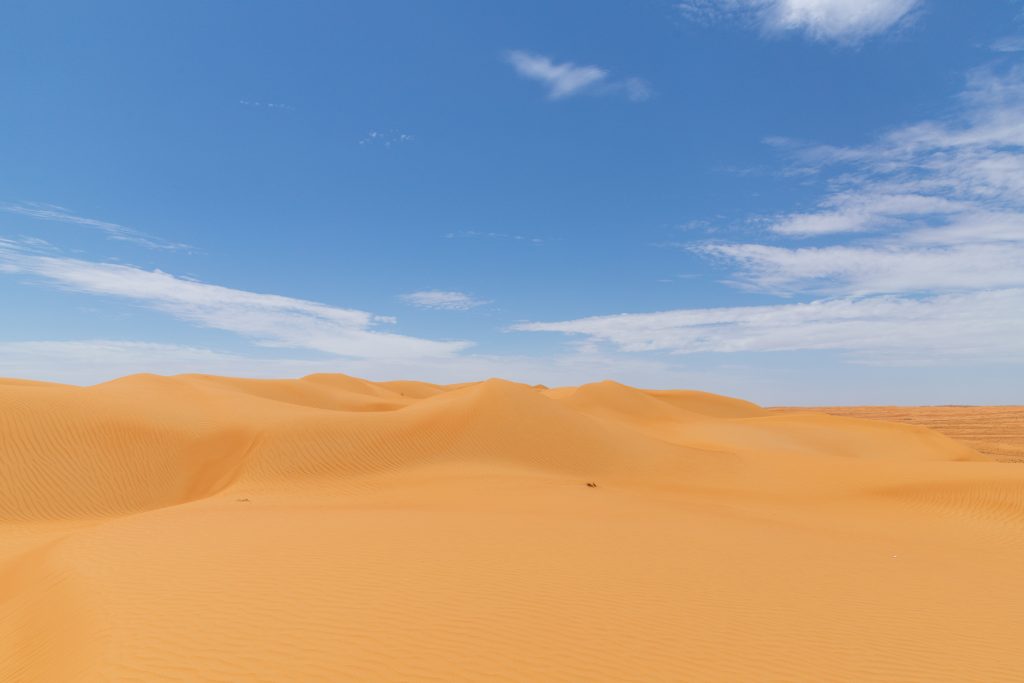 Bentang alam gurun Wahiba Sands di Oman dengan bukit pasir keemasan dan langit biru cerah.