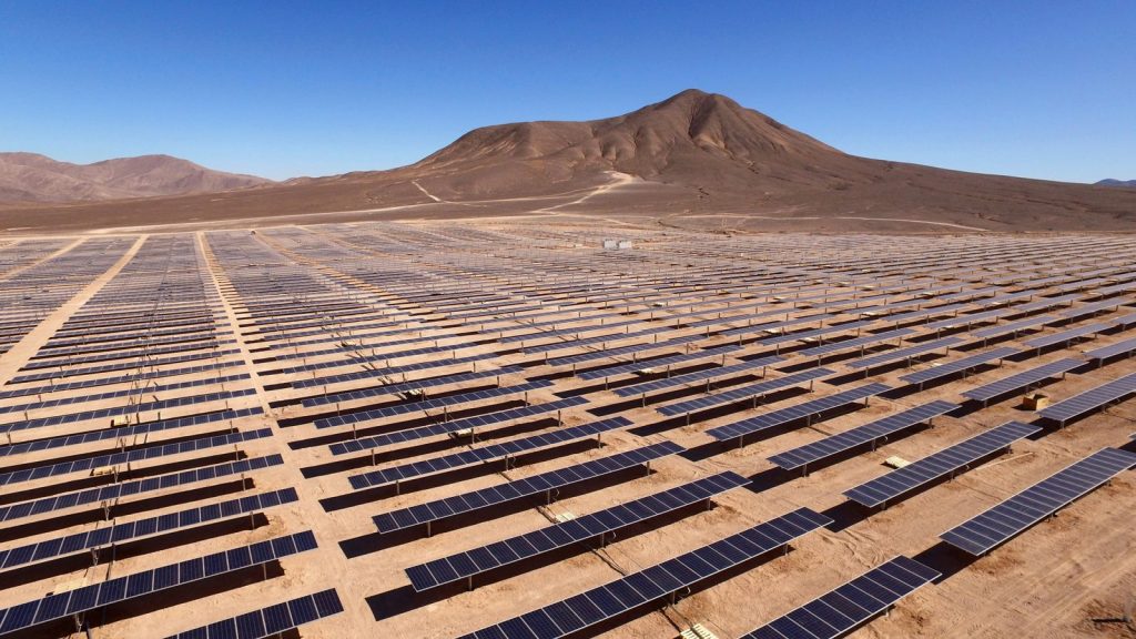 Solar panels stretching across a desert plain with mountains in the background.